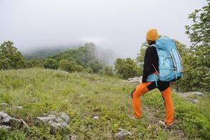 A man in sports equipment with a backpack on his back, a tourist on a hike looks at a landscape with a forest, the equipment of a guy on a trip, a hat on his head. photo