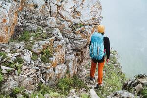 A view from behind a man with a backpack on a hike, a guy standing in the mountains in sports gear, a large backpack on his back, foggy weather in the mountains. photo