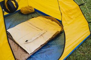 Tourist tent yellow inside view, sleeping bag lies on the mat, camping in the forest, a place to rest and sleep, equipment for hiking. photo