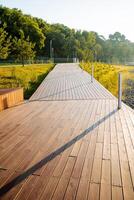 A road of boards, a pedestrian crossing, a wooden path, a city recreation park, the design of the coastal area, a well-groomed lawn. photo