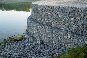 Stone embankment is a way to strengthen the river bank from collapse, gravel is poured into a metal mesh, the basis for concreting, construction work. photo