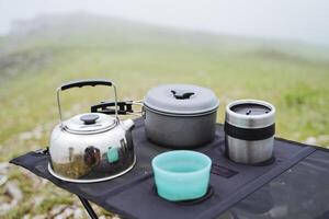 Camping utensils, a tourist metal kettle, a set of dishes, a glass of plastic, an iron pan. photo