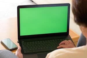 Green screen laptop computer closeup. Unknown senior lady having call at chroma key laptop screen at home. Unrecognizable elder woman making conference at mockup laptop photo