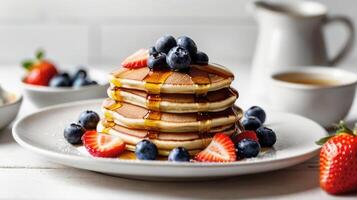 Delicious stack of pancakes topped with syrup and fresh berries, served on a white plate against a clean white table, perfect for a breakfast concept photo