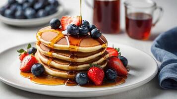 delightful breakfast scene with a stack of pancakes drizzled in syrup and adorned with strawberries and blueberries, elegantly presented on a white plate atop a pristine white table photo