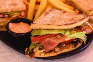 Close-up of club pita giros chicken with cheese, bacon, tomato, lettuce, sauce served with fries on the black plate on white background in greek tavern. Mediterranean cuisine. Selective soft focus photo