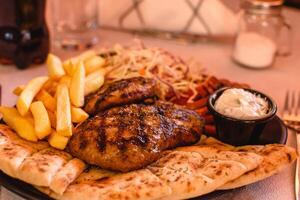 Burger, fries, pita, tomato, cabbage, sauce served on the black plate on white background in greek tavern. Mediterranean cuisine. Selective soft focus photo