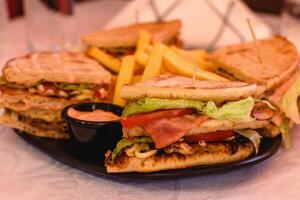 Club pita giros chicken with cheese, bacon, tomato, lettuce, sauce served with fries on the black plate on white background in greek tavern. Table setting. Mediterranean cuisine. Selective soft focus photo