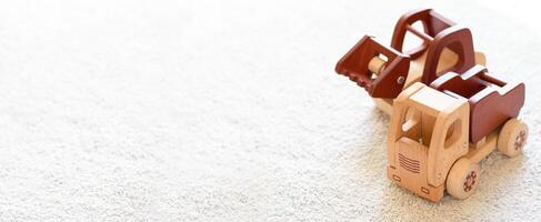 Banner with selective focus on wooden cars truck and bulldozer in natural colors on a white cotton carpet. Environmentally friendly, plastic free toys for toddler. Eco concept. Space for text photo