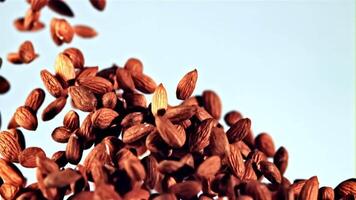 Slow motion shot of almonds falling onto a white background, eventually forming a pile. Additional shots show almonds falling in the air on both white and blue backgrounds High quality video