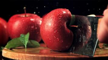 A ripe apple is cut into halves with a large knife. On a black background. Filmed is slow motion 1000 fps. video