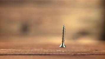 uno Autoperforantes tornillo caídas en el mesa. en un de madera fondo.filmado es lento movimiento 1000 marcos por segundo. alto calidad full HD imágenes video