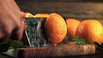 A man's hand cuts an orange into two pieces with a knife. On a wooden background.Filmed is slow motion 1000 fps. High quality FullHD footage video