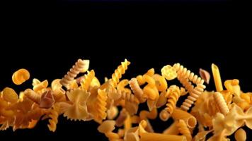 A variety of pasta types are scattered on a dark background. This macro photography showcases the beauty of each individual ingredient, ready to be used in a delicious cuisine dish or recipe video