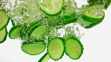 Slices of cucumber are gracefully sinking into the clear water, creating a visually appealing contrast against the white background video