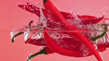 Capture the stunning moment of red peppers falling and splashing into water on a vibrant pink background. Colors pop in highspeed action, creating a visually appealing scene with fluid movements video