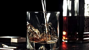 Super slow motion whiskey with splashes flows into a glass of ice. High quality FullHD footage video