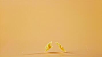 súper lento movimiento pasta farfalle caídas en el mesa. en un amarillo fondo.filmado en un alta velocidad cámara a 1000 fps. alto calidad full HD imágenes video