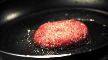 super lento movimento con un' spruzzo di olio fritte hamburger nel un' frittura padella. su un' nero sfondo.filmato su un' alta velocità telecamera a 1000 fps. video