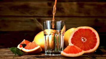 Super slow motion a jet of grapefruit juice pours into the glass. On a wooden background. Filmed at 1000 fps. video