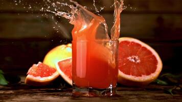 ein Super schleppend Bewegung Stück von Grapefruit Stürze in ein Glas von Grapefruit Saft mit Spritzer.gefilmt beim 1000 fps. auf ein hölzern Hintergrund. video