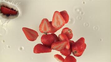 Super slow motion pieces of strawberries fall into the milk. On a white background. Filmed on a high-speed camera at 1000 fps. Top view video