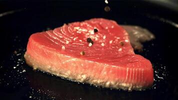 Super slow motion on the tuna steak in a frying pan drops black pepper. On a black background. Filmed on a high-speed camera at 1000 fps. video