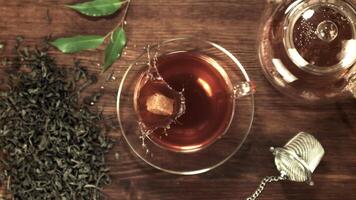 Super slow motion a piece of cane sugar falls into the tea with splashes. On a wooden background.Filmed on a high-speed camera at 1000 fps. Top view. video