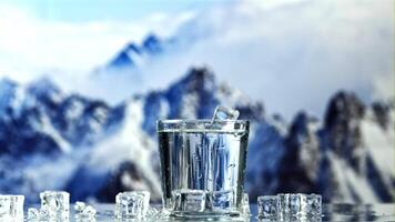 Ice cubes with splashes fall into a glass of water. Against the backdrop of mountains. Filmed is slow motion 1000 fps. video