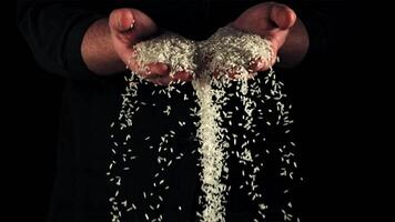 Uncooked rice falls from men's hands. On a black background. Filmed on a high-speed camera at 1000 fps. video