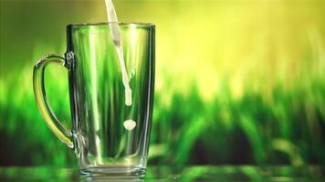 A stream of milk pours into a mug of spray. Against the backdrop of green grass. Filmed on a high-speed camera at 1000 fps. video