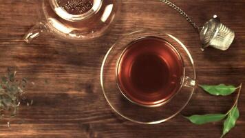 súper lento movimiento seco té hojas otoño en el mesa siguiente a el té en el taza. en un de madera antecedentes. parte superior vista. filmado en un alta velocidad cámara a 1000 fps. video