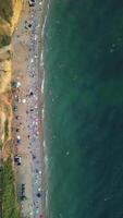 antenne visie van zanderig strand, zwemmen mensen in zee baai met transparant blauw water Bij zonsondergang in zomer. gelukkig mensen menigte ontspannende Aan strand. vakantie recreatie oceaan natuur concept. verticaal video