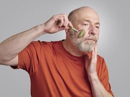 senior man is using a jade stone roller for a face massage photo