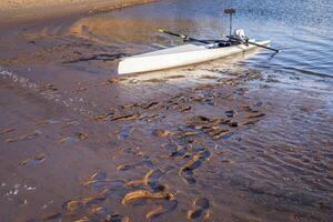 Coastal rowing shell on a muddy shore of Carter Lake in northern Colorado with footprints photo