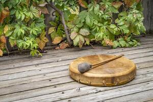 handmade, native American style, shaman frame drum covered by goat skin with a beater on a rustic wooden backyard deck photo