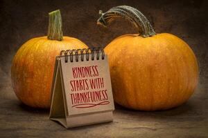 Kindness start with thankfulness - handwriting in a desktop calendar with pumpkins, November and Thanksgiving season concept photo