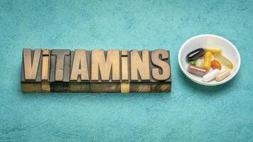 vitamins word in vintage letterpress wood type with a small bowl of pills and capsules, healthy lifestyle concept photo
