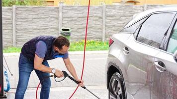 Young man washes his car at a self-service car wash using a hose with pressurized water and foam. High quality 4k footage video