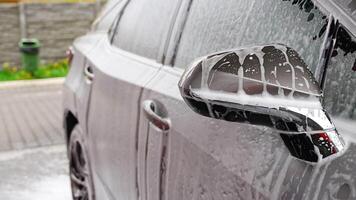 Teil von Auto während Waschen mit Shampoo, Wasser und Schaum tropft von das Wagen. hoch Qualität 4k Aufnahmen video
