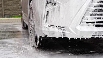 een deel van auto gedurende het wassen met shampoo, water en schuim druipend van de auto. hoog kwaliteit 4k beeldmateriaal video