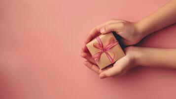 A person is holding a small gift box with a red ribbon on peach background photo