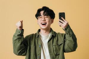 Portrait of excited happy young man holding mobile phone isolated on yellow background. Copy space photo
