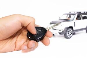 Car key in hand with toy car on the background isolated on white. Car stuff concept. After some edits. photo