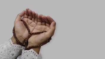 Muslim praying hands holding prayer beads in Ramadan, isolated gray background photo