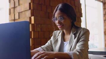 giovane indiano donna utilizzando il computer portatile computer nel bar. femmina professionale Lavorando con taccuino video