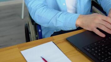 maschio alunno apprendimento in linea utilizzando il computer portatile digitando seduta nel sedia a rotelle nel appartamento occupato con lontano formazione scolastica. tecnologia e invalidità concetto video