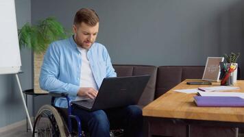 mannetje leerling aan het leren online gebruik makend van laptop typen zittend in rolstoel in appartement bezig met ver weg onderwijs. technologie en onbekwaamheid concept video