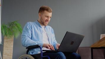 portatori di handicap libero professionista è Lavorando con il computer portatile digitando seduta nel sedia a rotelle a ufficio. lontano opera e invalidità concetto video