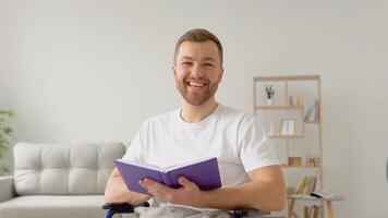 Cheerful happy disabled person reading a book in a wheelchair and looking at camera video